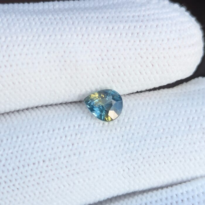 Teardrop-shaped teal sapphire gemstone on fabric